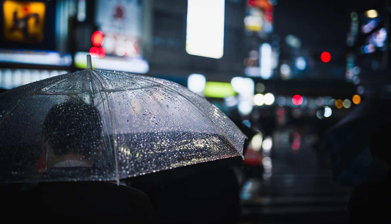 Man walking with a transparent umbrella in a city at night showing cyber insurance coverage for nation-state attacks