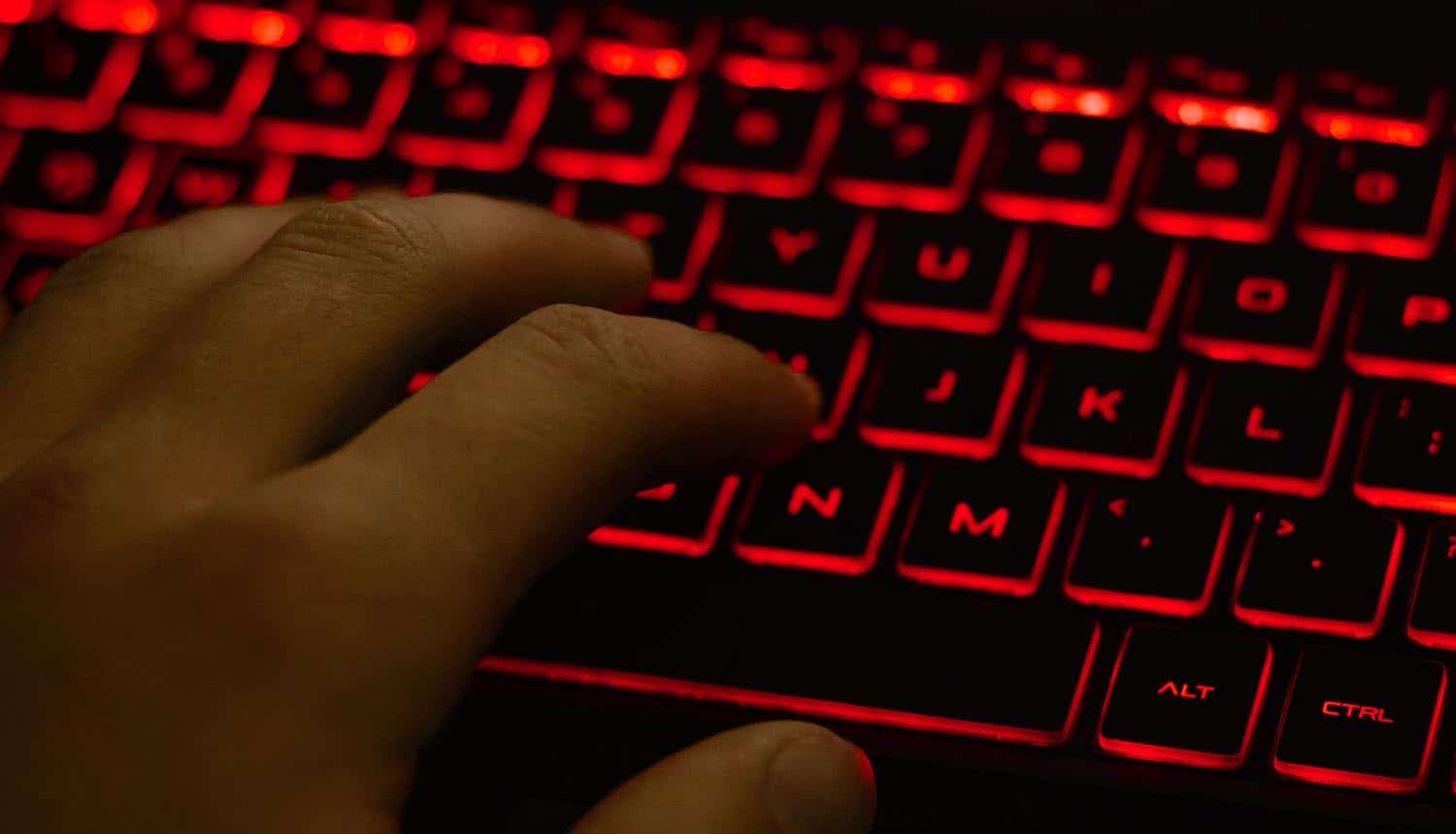 Man's hand typing on keyboard with red backlight showing ransomware attack