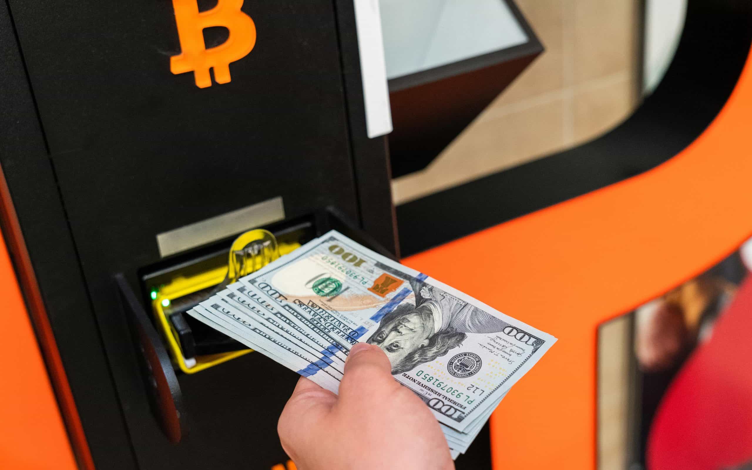 Hand inserting dollar bills in bitcoin ATM showing crypto theft