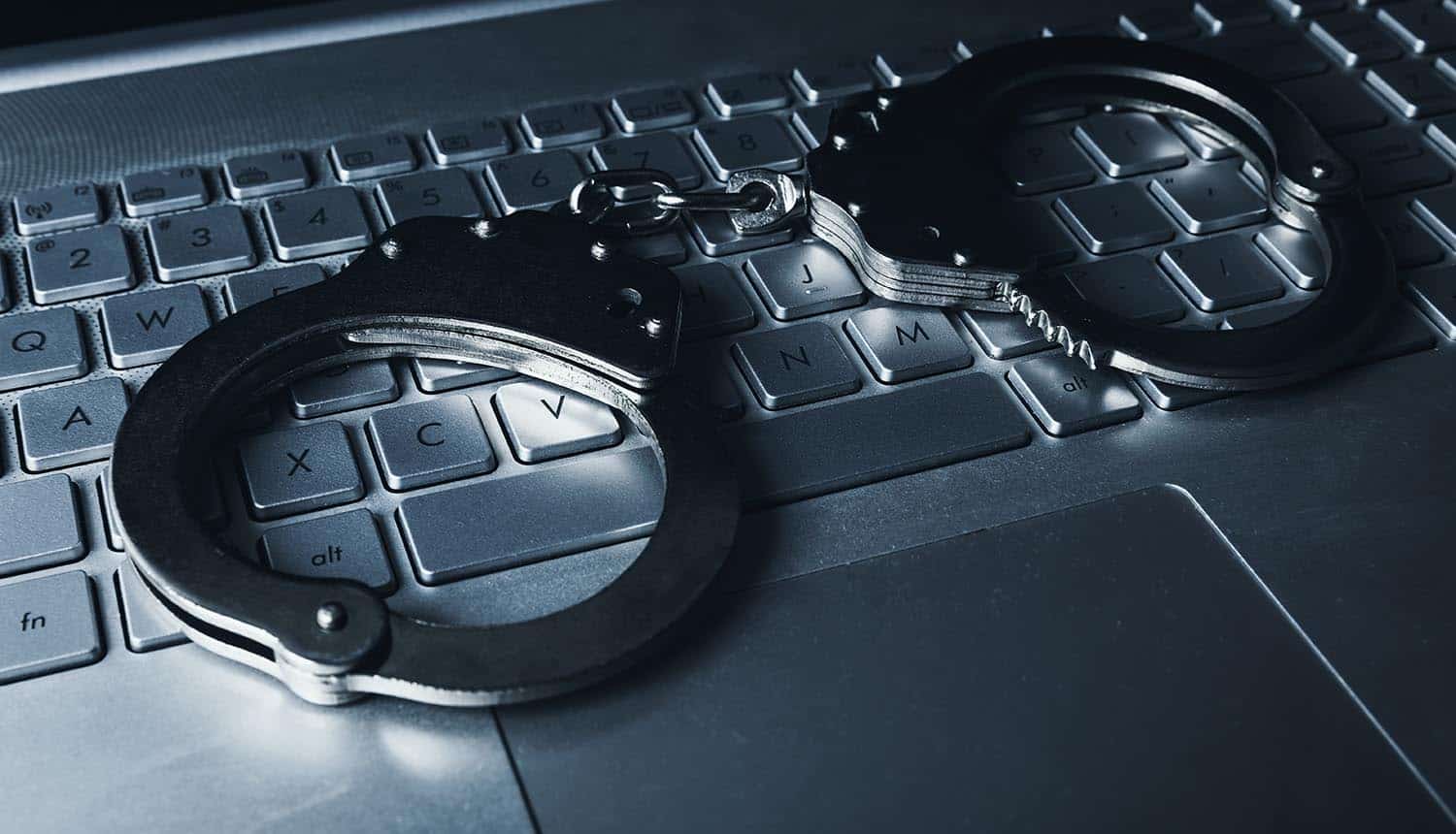 Handcuffs on laptop keyboard showing international law enforcement operation on dark web market