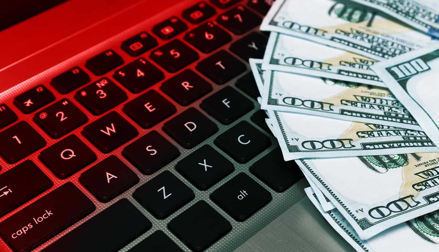 Computer keyboard with dollar bills and red light showing operating expenses of cyber crime groups