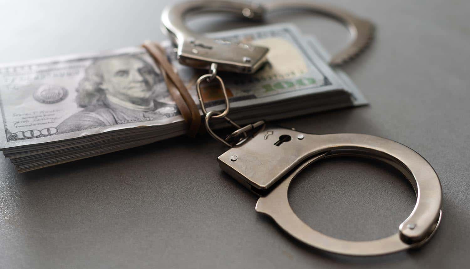 Handcuffs on hundred-dollar bills showing Reward for Justice bounty for Clop ransomware