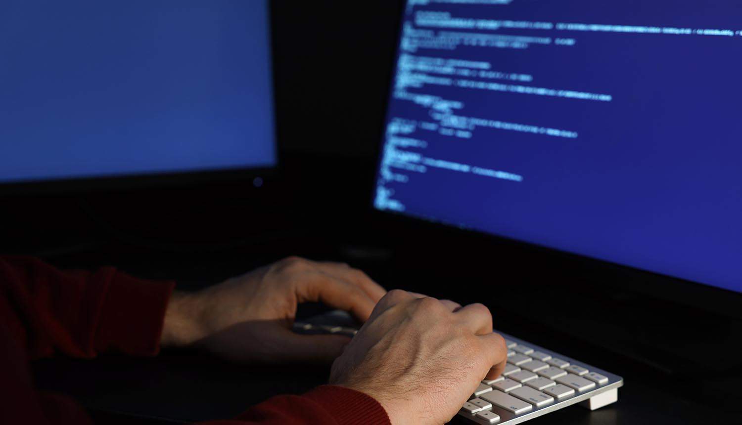Hacker working with computers in dark room showing China cyber attacks by U.S. intelligence agencies