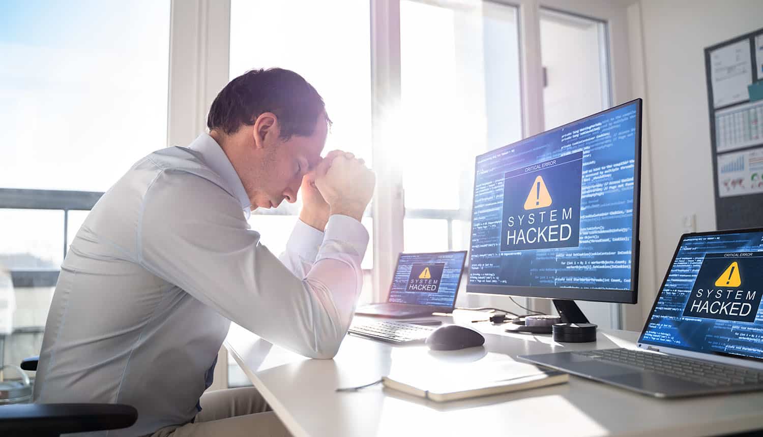 Man in front of monitor with system hacked sign showing cost of data breach