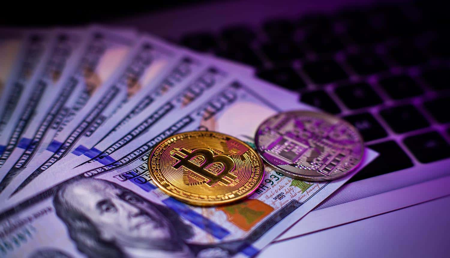 Bitcoin on a laptop keyboard and hundred-dollar bills showing crypto company crypto hack