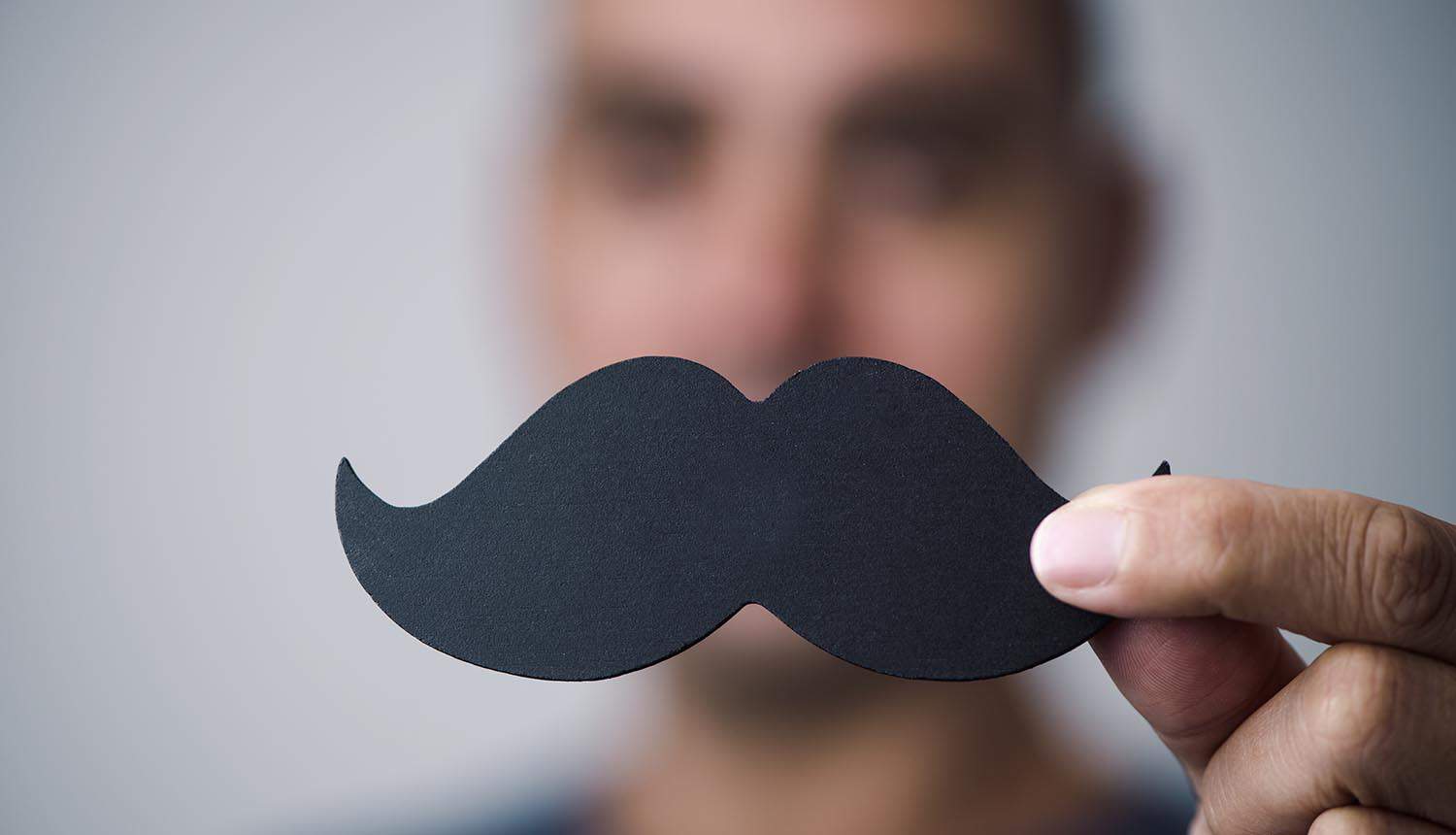 Man holding a fake moustache in front of his face showing deepfake scam fraud